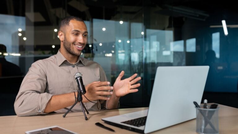 Successful hispanic man inside office with professional microphone recording audiobook and online podcast, business coach work with laptop live event Businessman in casual shirt glasses at workplace