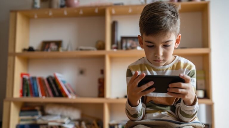 one boy caucasian child preschooler hold smartphone mobile phone at home play video games childhood and growing up technology addiction concept use smartphone app for online browsing or watch video