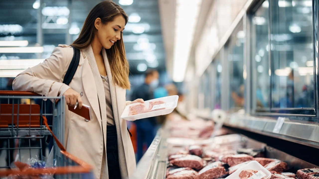 Young happy woman choosing fresh meat while buying food at the supermarket.