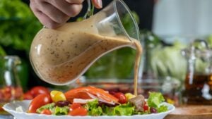 woman chef mix fresh baby cos salad and pour salad dressing in glass blow. Organic Vegetables mix all green salad In glass bowl. Breakfast fresh salad and clean vegetable.