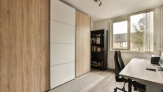 a home office with wood paneled walls and white cabinets on the wall, there is a large window that looks out onto the