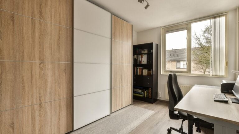 a home office with wood paneled walls and white cabinets on the wall, there is a large window that looks out onto the
