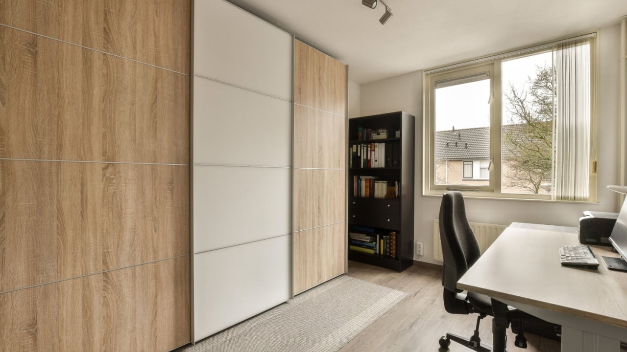 a home office with wood paneled walls and white cabinets on the wall, there is a large window that looks out onto the