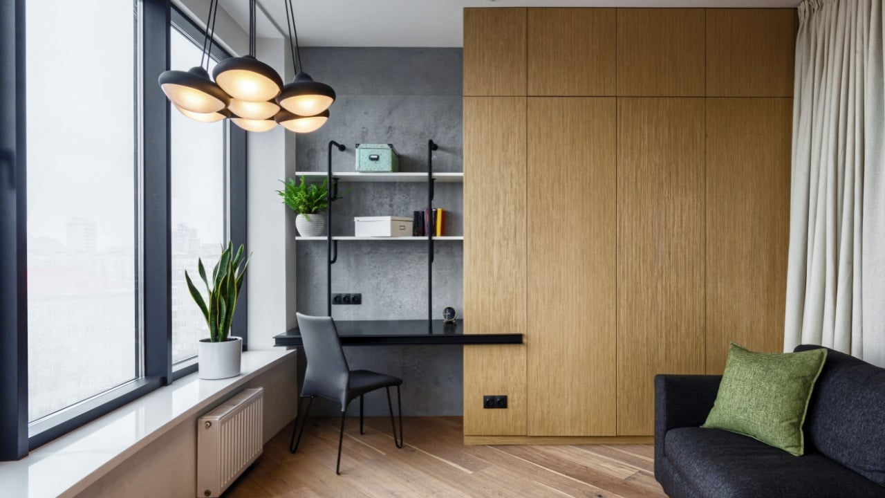 room with wooden wardrobe and cushion on grey comfort couch. home office with desk and chair near window. concept of modern interior in stylish apartment