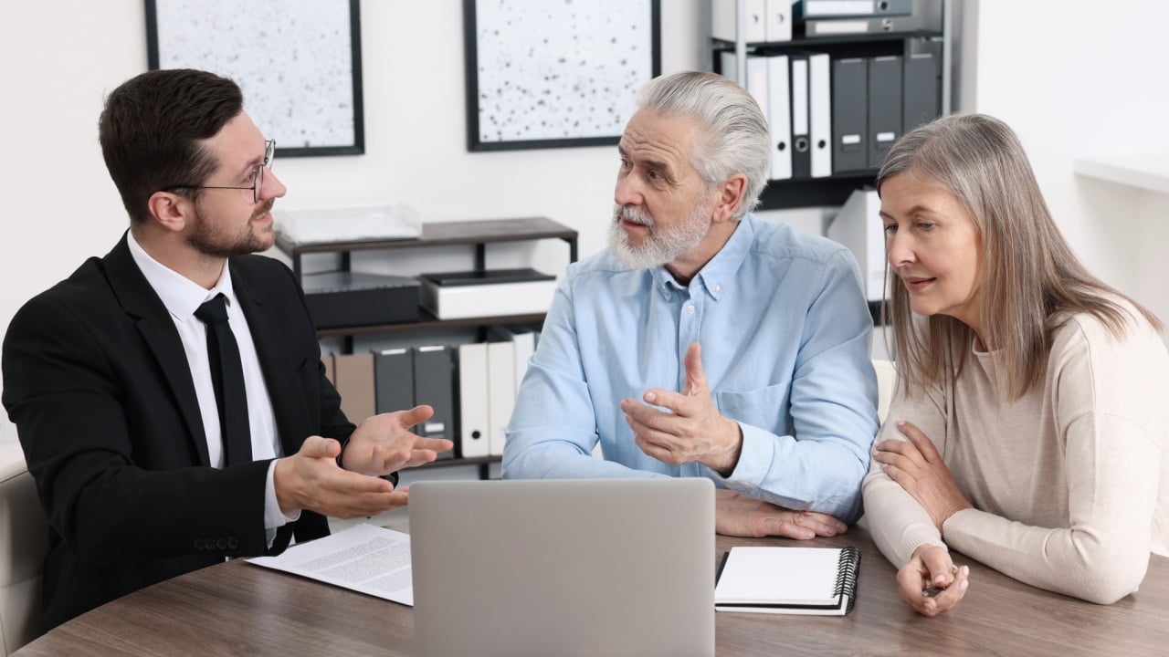 Insurance agent consulting elderly couple about pension plan at wooden table in office