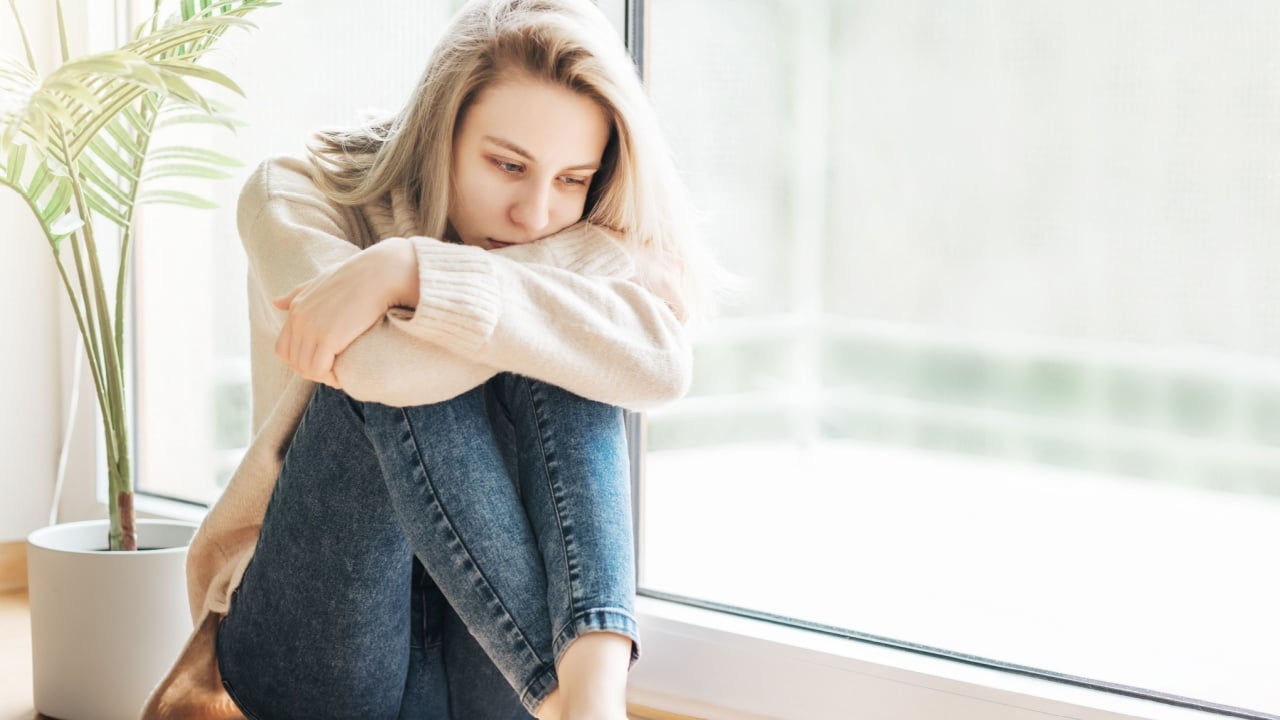 Sad girl near window thinking about something. Stressed lady feel lonely