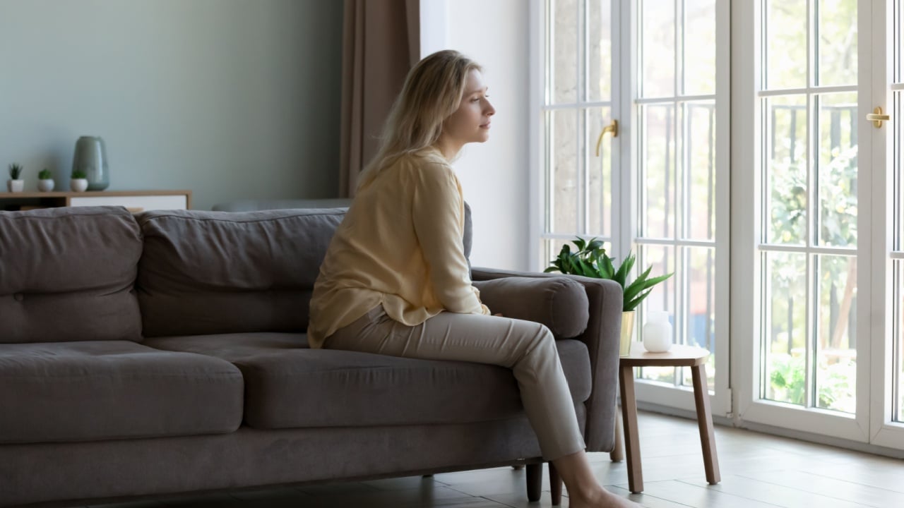 Thoughtful pretty young woman sitting on sofa indoors, looking away, thinking over bad concerning news, problem, troubles, feeling worried, lonely, making difficult decision