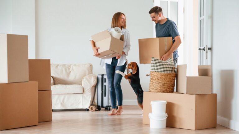 Two boxes in hands. Young couple with dog are moving to new home.