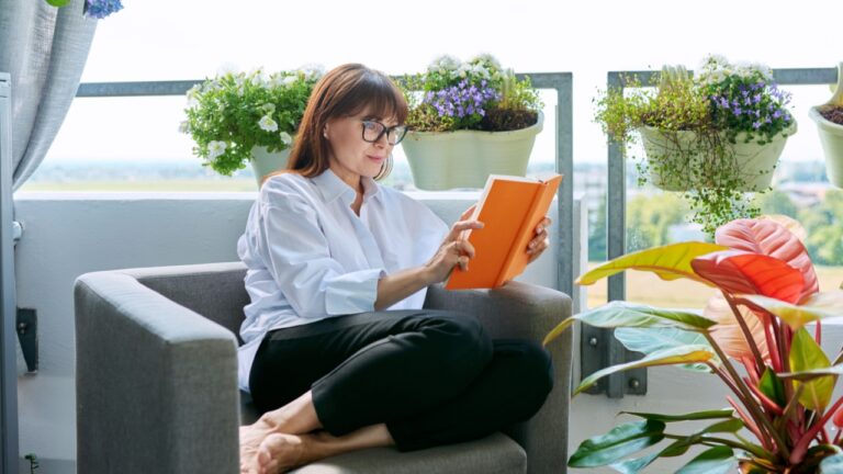 Middle-aged relaxed happy woman reading book, sitting at home