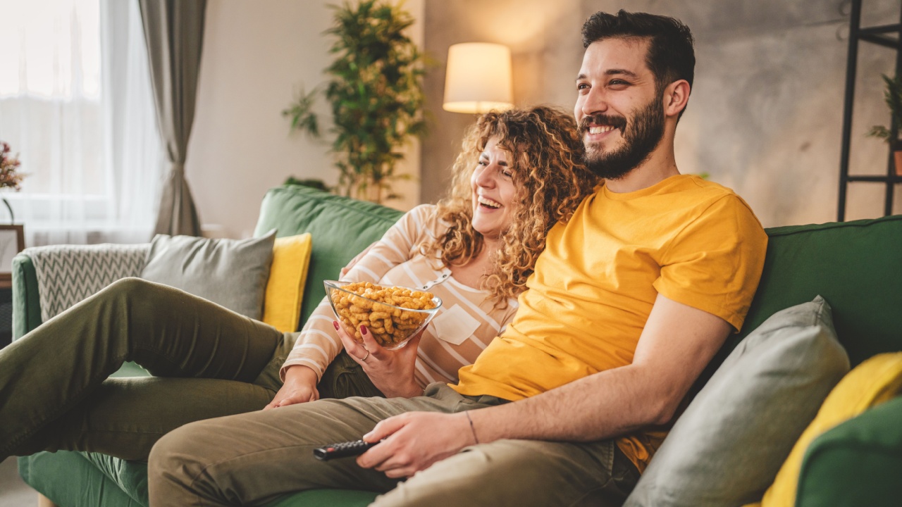 Couple man and woman caucasian husband and wife or boyfriend and girlfriend sit on the sofa bed at home watch tv movie series with hold remote controller happy smile bonding love family concept