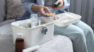Woman putting pills into first aid kit indoors, closeup