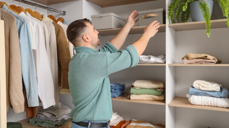Young man taking box from shelf in walk-in closet
