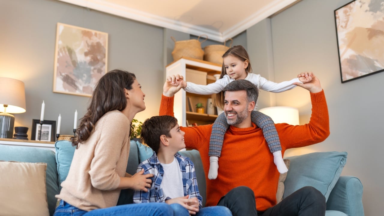 Cheerful family sitting on couch in living room have fun little daughter and son laughing together with parents enjoy free time playing at home. Weekend activity happy family