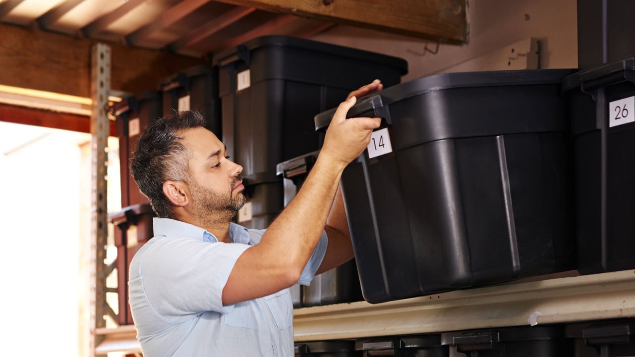 Box, shelf and storage with man in garage of home for cleaning, neat organizing or packing. Busy, container and plastic with confident mature person in home to arrange or order shelving in carport