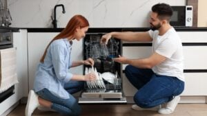 Lovely couple loading dishwasher with plates in kitchen