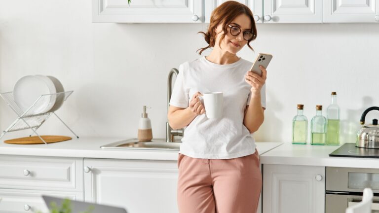 Middle-aged woman stands in kitchen, holding phone.