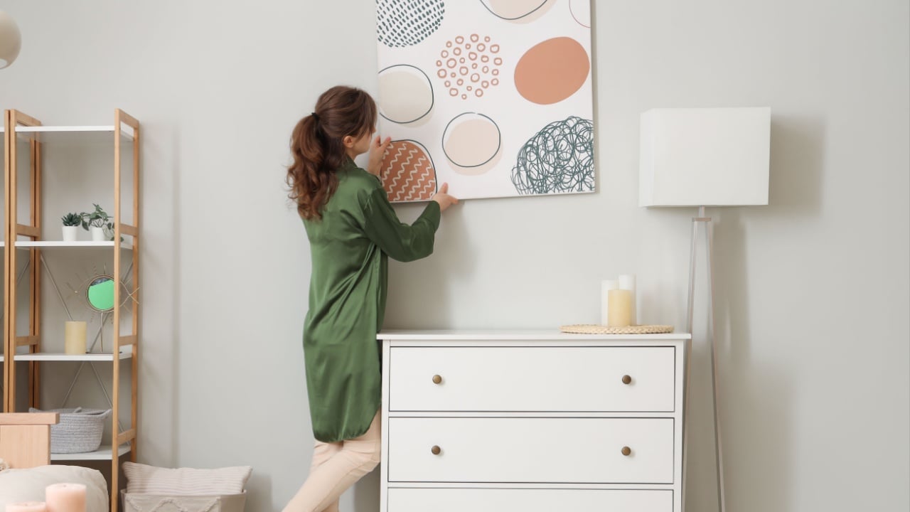 Young woman hanging picture in stylish living room
