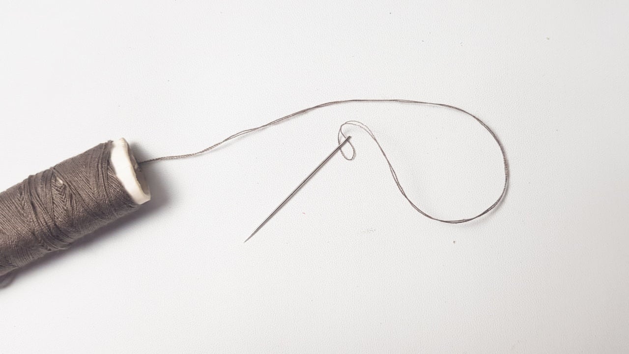 A spool of brown sewing thread with a needle next to it isolated on a white background