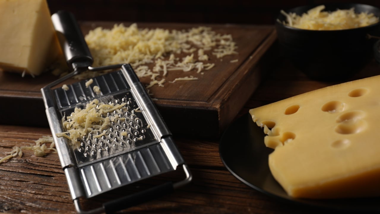 Different types of cheese and grater on wooden table, closeup