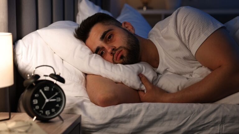 Frustrated man suffering from insomnia on bed