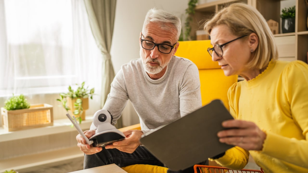 Couple at home mature or senior caucasian husband and wife connect and install cctv security surveillance camera