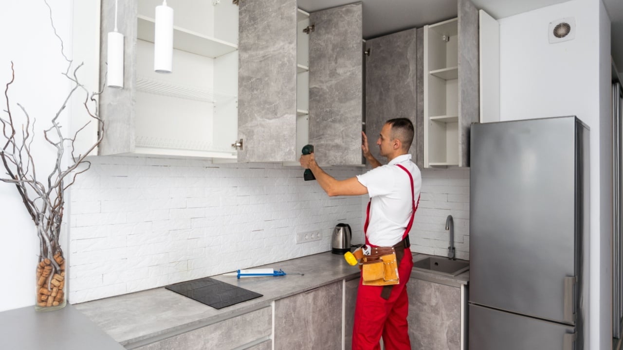 Worker installing door of cabinet in kitchen