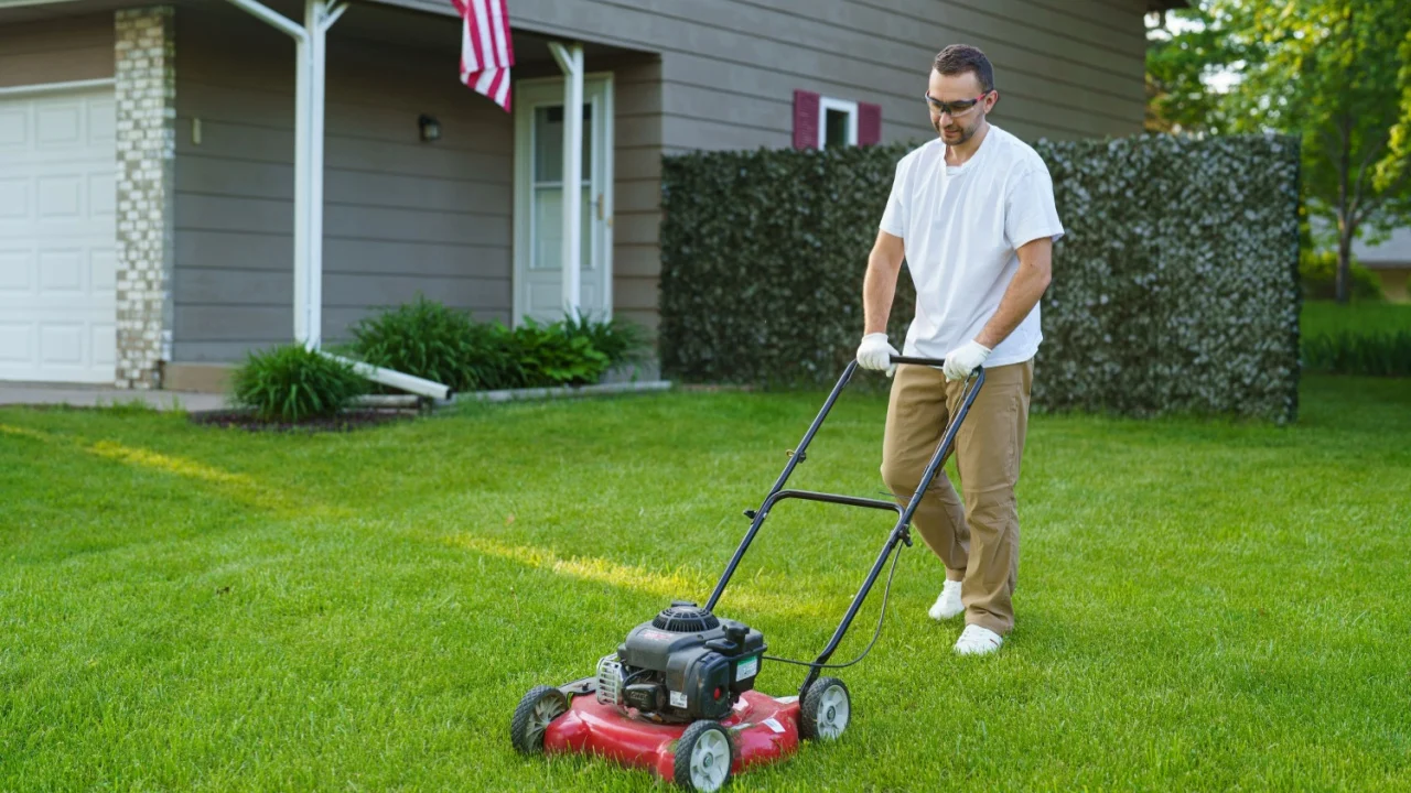 Smiling man standing with lawnmower in garden