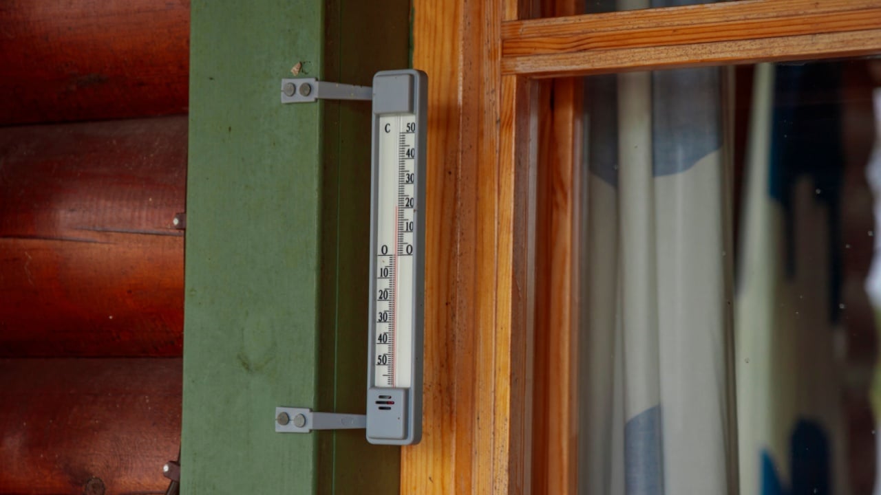 Outdoor thermometer outside the window of the wooden house is close-up. Thermometer scale with plus air temperature. A device for determining the air temperature outside the house