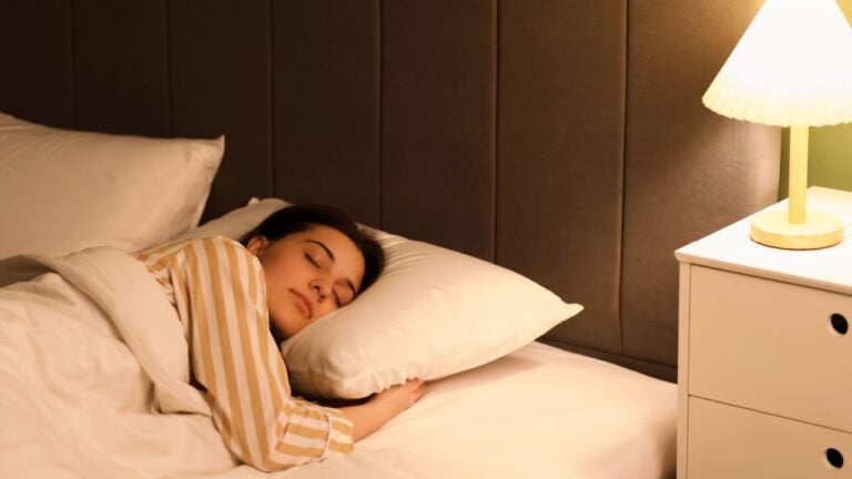 Young woman in pajamas sleeping on cozy bed in bedroom at night