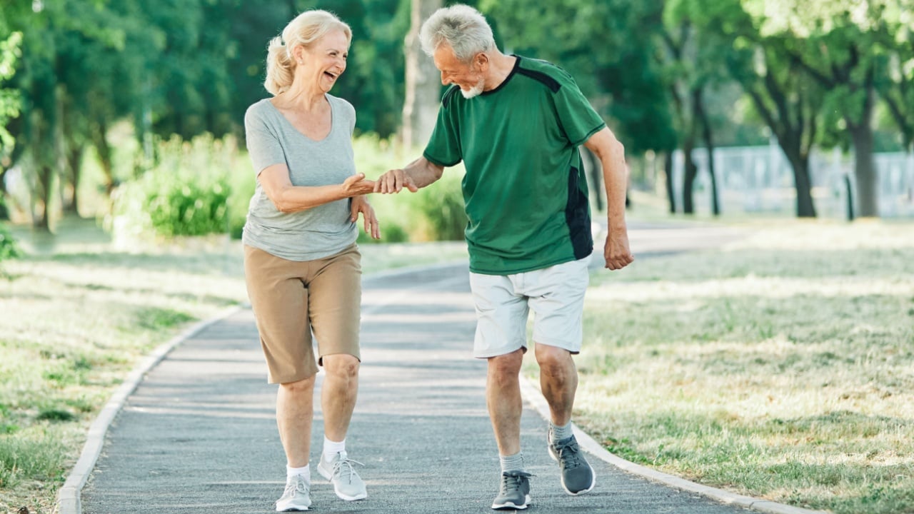 Smiling active senior couple jogging exercising and having fun and celebrating success raising hands together taking a break in the park