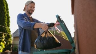 Man throwing trash bag full of garbage into bin outdoors