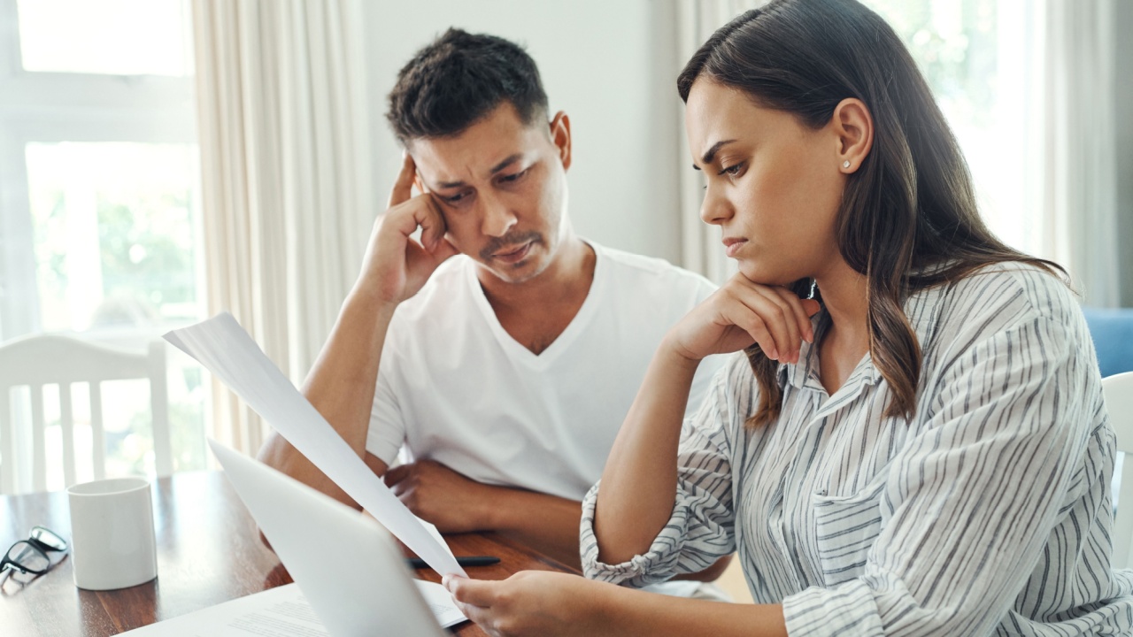 Laptop, documents and confused couple in home for budget problem, mortgage debt and financial risk. Computer, man and woman with stress for tax paperwork, low credit score and inflation for expenses