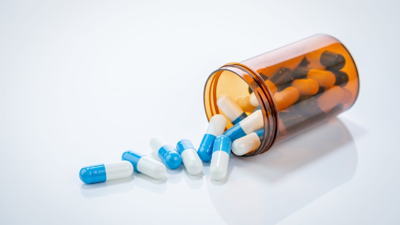 Prescription antibiotic capsules spilling from amber bottle on white background. Blue and white capsule pills. Healthcare and pharmaceutical. Medical treatment pills. Pharmacy and medicine industry.