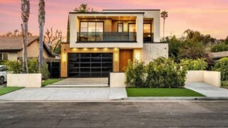 Modern two-story house with large windows and a landscaped front yard at sunset.