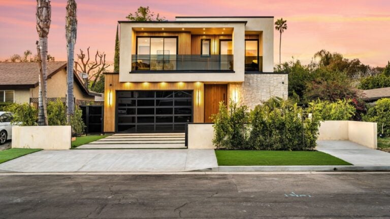 Modern two-story house with large windows and a landscaped front yard at sunset.