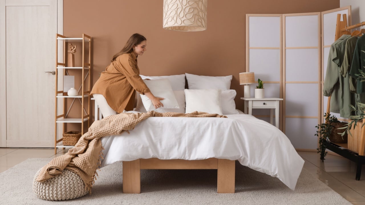 Pretty young woman making bed in modern bedroom