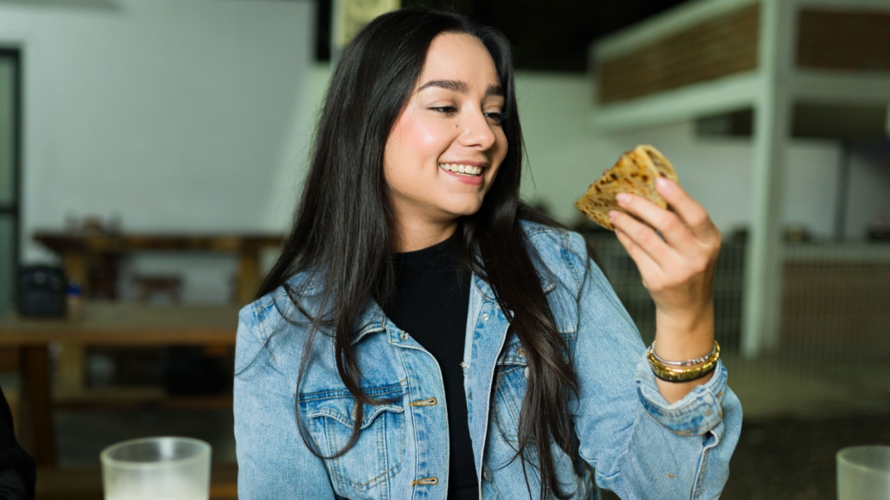 Happy young woman eating a delicious quesadilla at a mexican taco shop restaurant