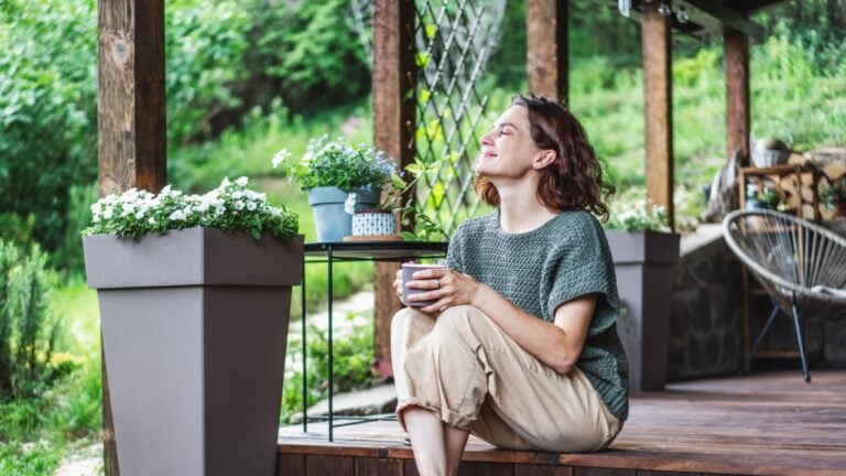 Young happy smiling Caucasian woman sitting on the wooden terrace of a country house enjoying the summer weather