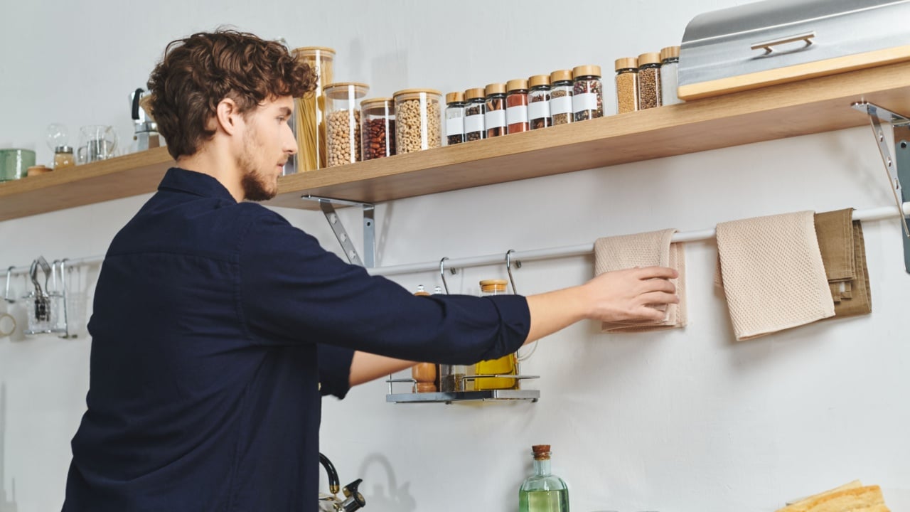 Handsome curly-haired man organizes kitchen items in his modern and spacious apartment.