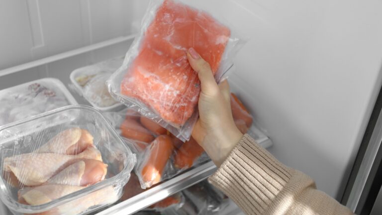 Woman taking frozen piece of salmon out of fridge, closeup