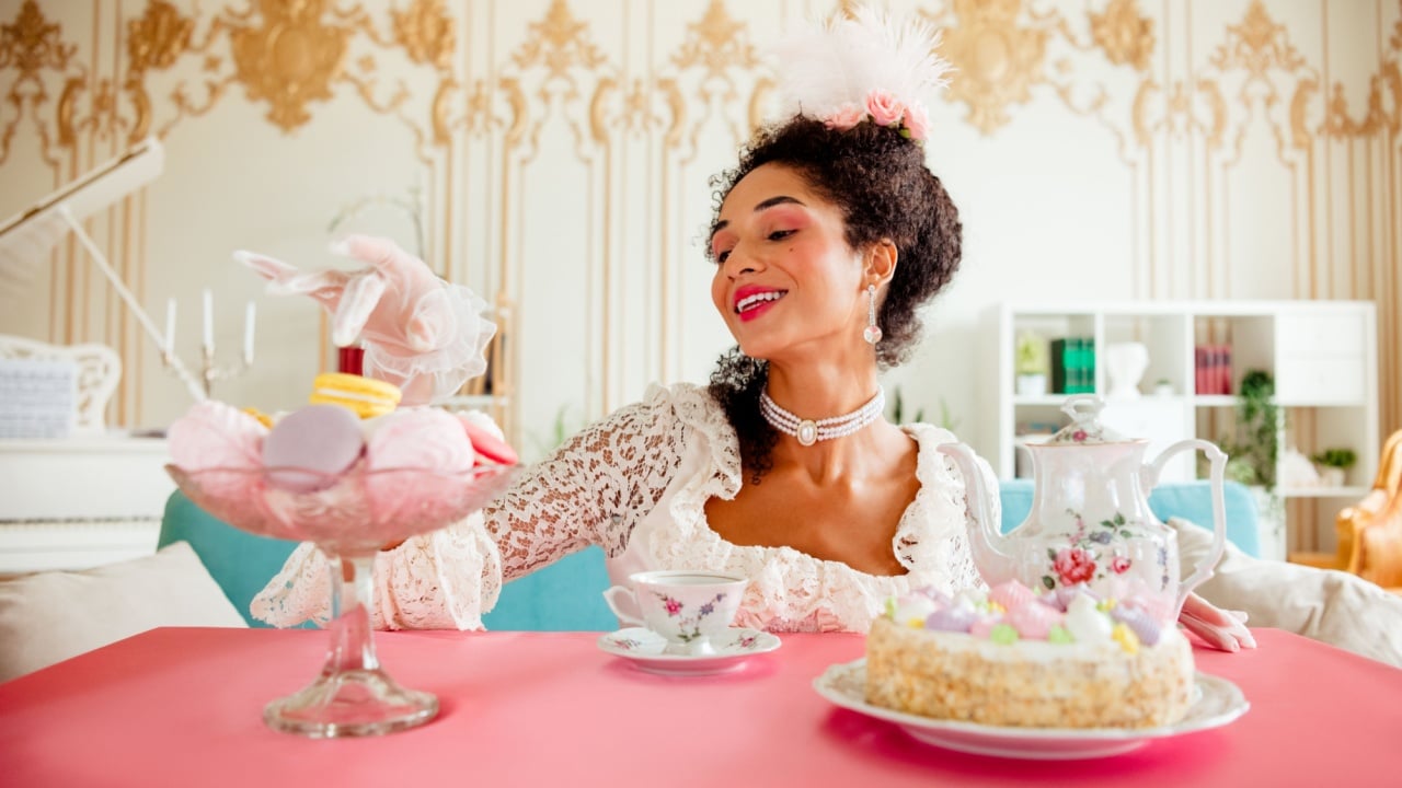 Elegant young woman dressed in baroque style enjoying tea and pastries in a luxurious interior
