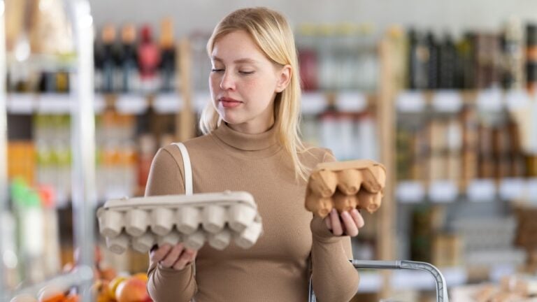 Girl buyer choosing compare varieties eggs, doubt and think before buying. Client look package of eggs, inspect product and examines contents of package