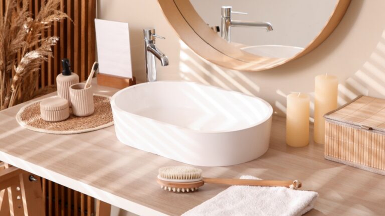 Table with sink, box and bath supplies near beige wall in bathroom