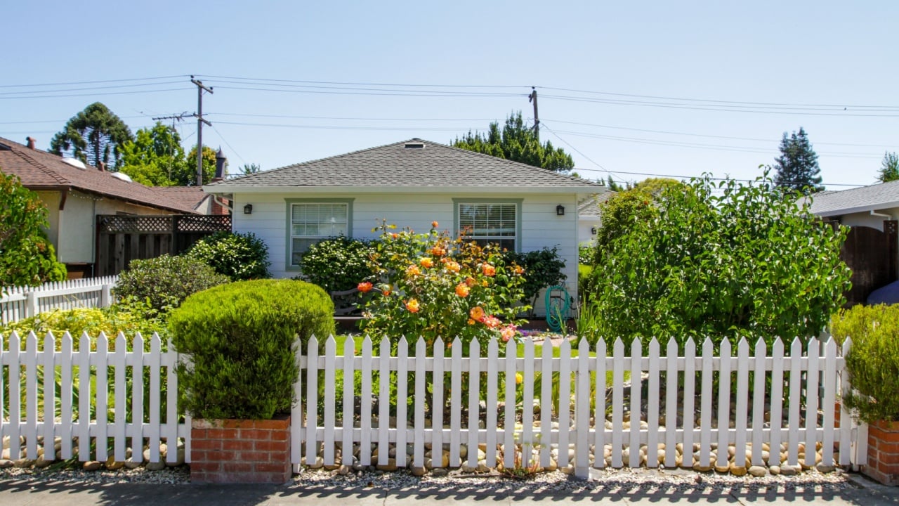 Front yard of a typical American small house, with nice landscaping, lush greenery, small white wooden fence, on a sunny day, no people. Typical American suburban residential area in a small town, CA california