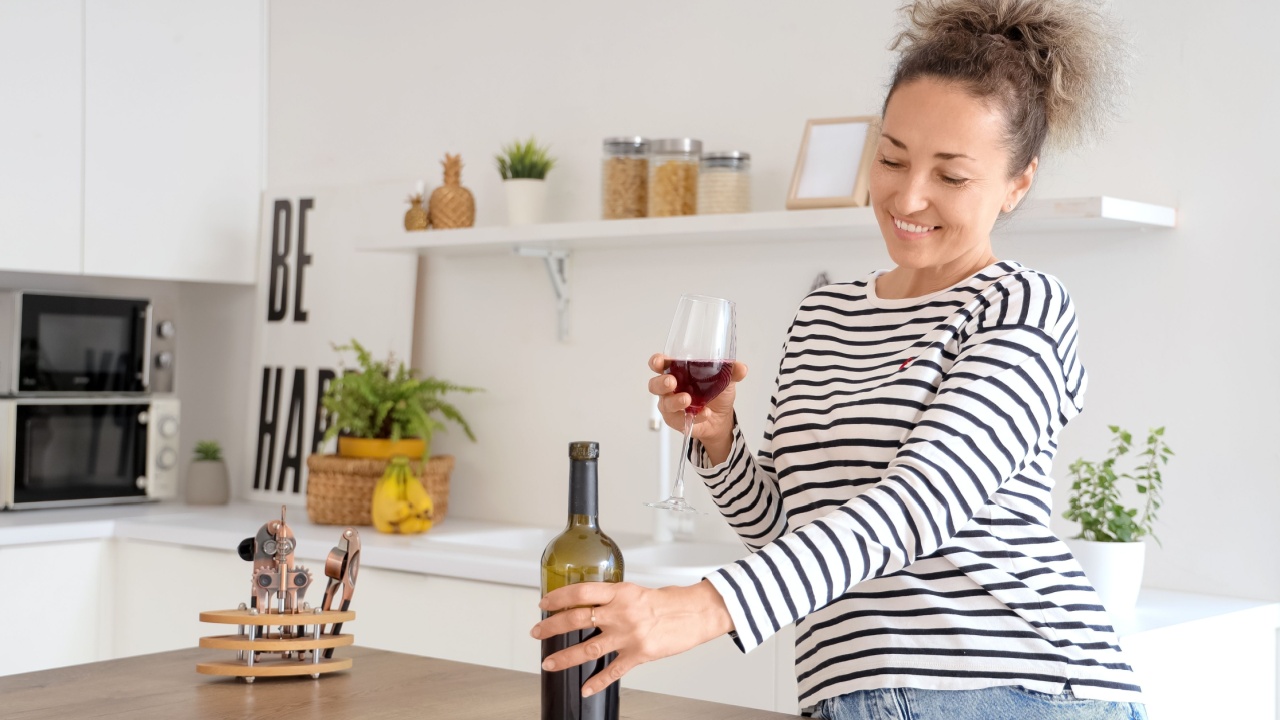 Beautiful middle-aged woman with bottle and glass of red wine at home