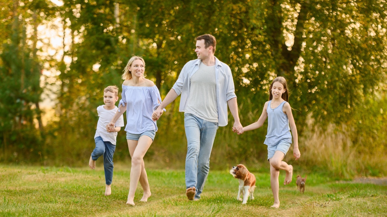 Family having fun outdoors running barefoot on grass, holding hands, laughing, with dogs running nearby. Summer weekend, country vacation concept. International Family Day