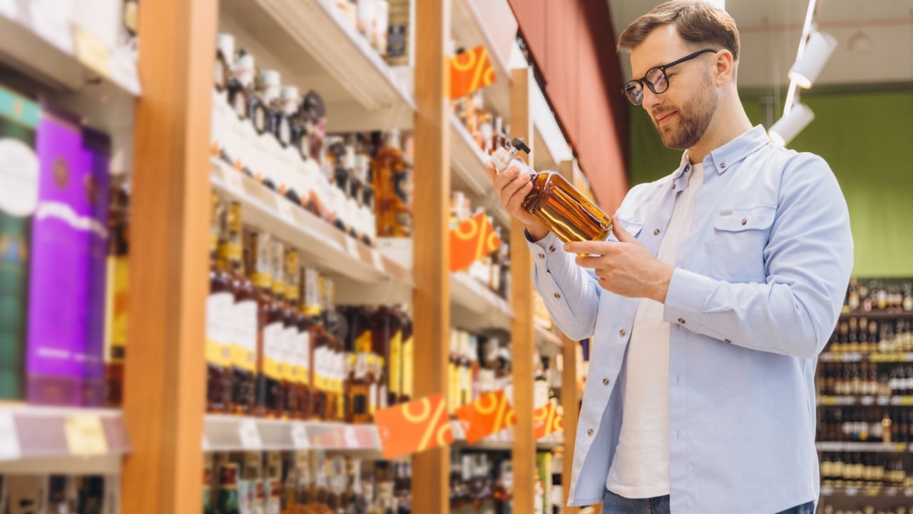 Man reading label of liquor bottle while shopping in grocery store