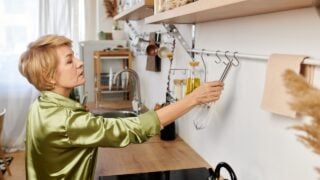 A lovely senior woman places a whisk on the rack, savoring the soft morning light.