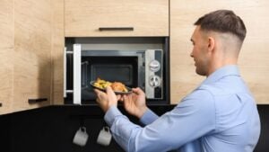 Man putting plate with lunch into microwave in kitchen