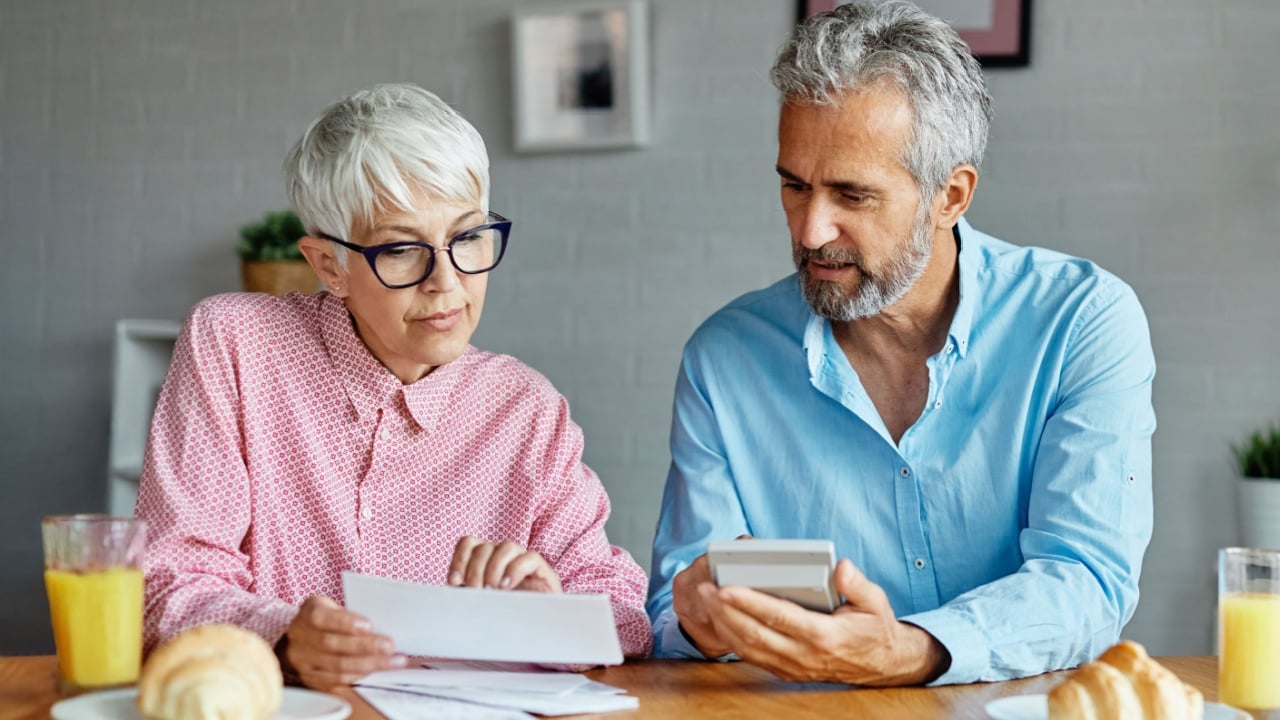 Senior couple checking bills and calculating expenses using a calculator at home, debt taxes and home budget concept, worried or a business meeting in office, businessman and businesswoman